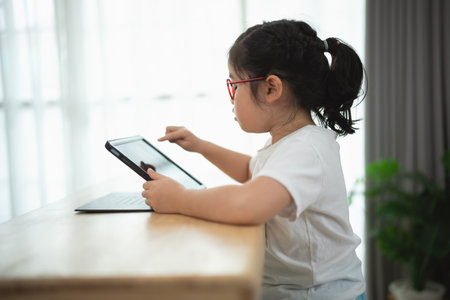 Young Girl Engaged with Tablet in Bright Room by Windowの写真素材