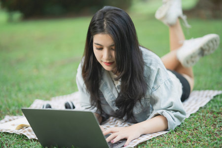 Young woman working on laptop in a peaceful park setting, surrounded by greenery, enjoying leisure...