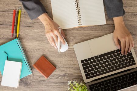 Top view of a business desk with hands typing on laptop keyboard with multi-colored pens, notebooks, business card bag and mouse, on a wooden table to connect with others in the digital technology world.の写真素材