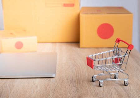 Mock up photo for e-commerce and online shopping from home or anywhere in the digital world. You'll see computer laptops, shopping trolley and many package boxes with the sun light and copy space.の写真素材