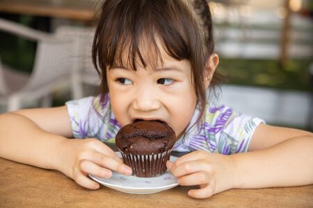 An Asian girl, about 3 years old eating a cake as a delicious snackの写真素材