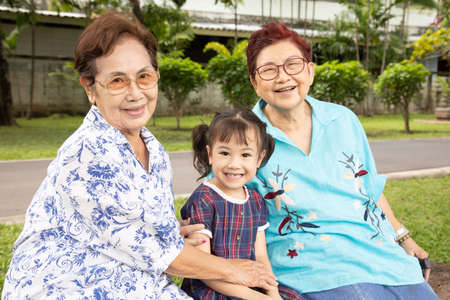Close up family shot of two grandmothers and their adorable granddaughter posing happily in the park outdoor shows positively smiling faces of senior persons having fun with kidin casual style.の写真素材
