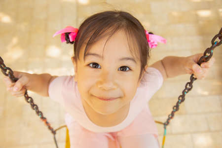 Top view and selective focus shot of adorable girl kid in pink ballet costume in playground looking up with pretty and lovely smile shows happiness of children and colorful life through her eyes.の写真素材