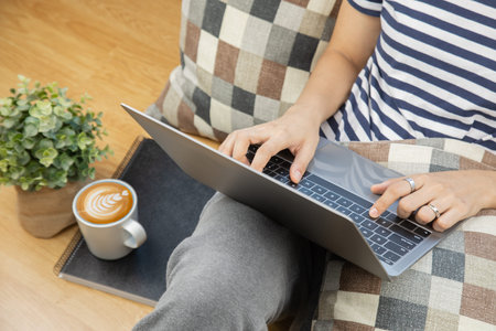 Lay flat view of asian woman working at home with laptop and black coffee on wooden floor shows...