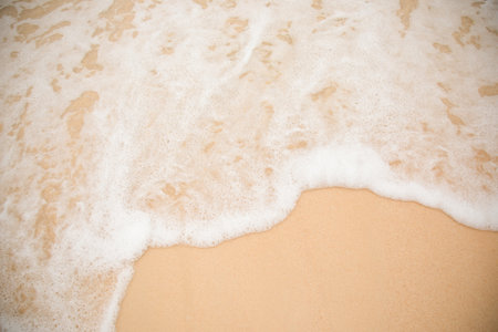 Close up and top view of glitter clear yellow sand on beach with water wave and white bubble shows beauty of natural vacation place in summer time under sunlight. It shows clear sandy texture surface.の写真素材