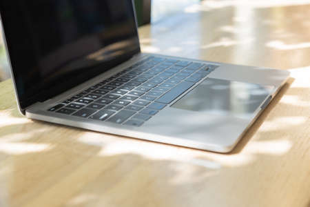 Selective focus with copy space of computer laptop or notebook on wooden table near window with beautiful sunlight in morning shows concept of work space from anywhere using internet technology.の写真素材