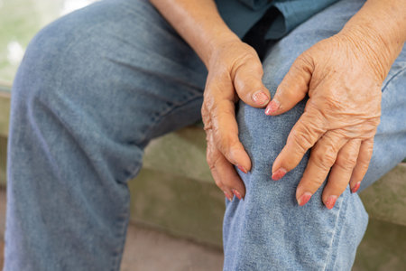 Close up shot of 80 years old woman sitting and touching her knees with hands due to feeling pain...