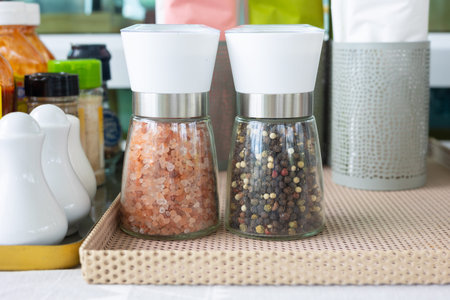 Close up and selective focus shot of two bottle of pink salt and pepper in containers with grinder...