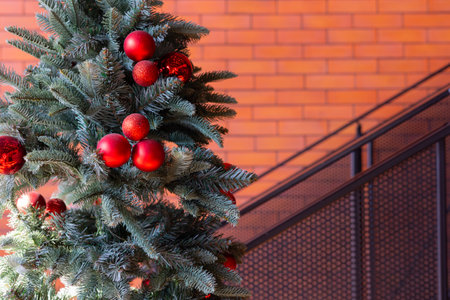 Christmas tree with decoration on red and sparkling ball with copy space of blurred background of brick wall and urban style stairway shows beautiful festival and celebration background.の写真素材