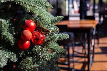 Close up Christmas tree with decoration on red and sparkling ball with copy space of blurred background of wooden decorated shop or store with desk and chairs shows beautiful festive background.の写真素材