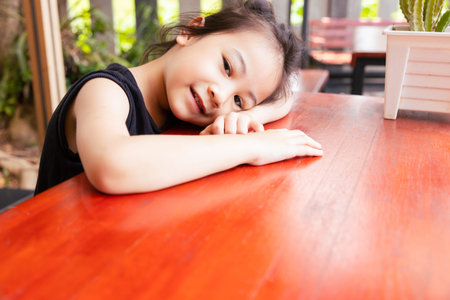 Close up face with copy space of adorable asian girl kid who is happily sleeping alone on the table outside shows concept of happy and cheerful emotion with smiling and relaxing.の写真素材