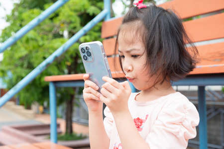 Adorable asian girl is using smartphone alone at school which is digital lifestyle of the kid to use technology for her communication, learning and entertainment. It is beautiful shot with copy space.の写真素材