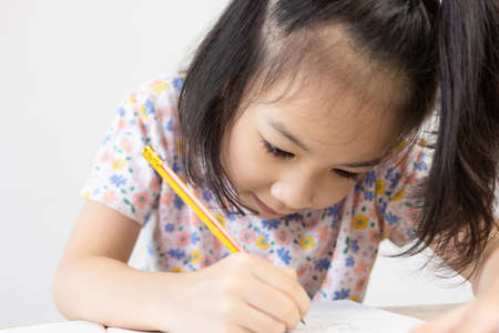 Close up shot of adorable child's face which are writing, reading and coloring on her book on the table. It is a concept of kid studying and learning with attention and concentration for education.の写真素材