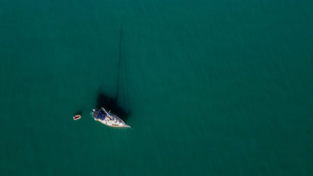 The drone captures a high angle view of cmonohull sailboat moored in a tranquil bay.
