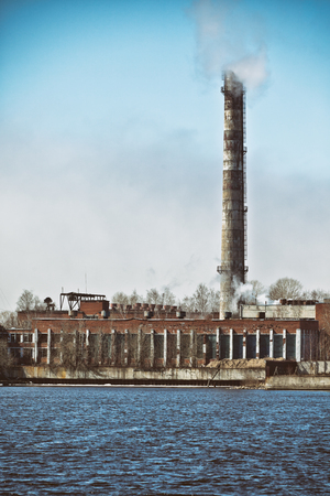Smoke emissions into the atmosphere from an old industrial pipe against a clear blue skyの写真素材