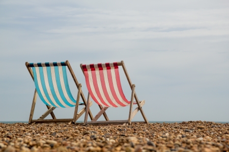 Landscape shot of 2 stripy deck chairs on a shingle beach in England looking out to seaの写真素材