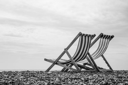 A low-angle monochrome shot of a pair of deck chairs looking out to sea