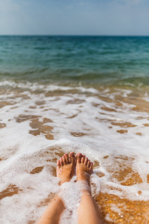Girls legs in the sea water on the sandy shore