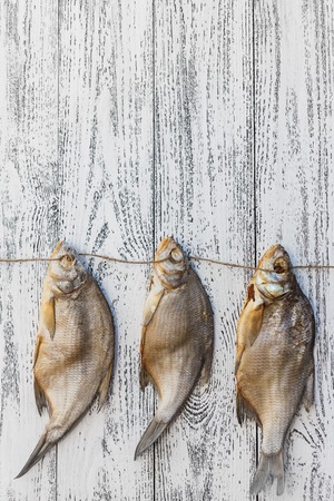 Three dried fish bream lie on a light wooden table. Fish hung on a rope.の写真素材