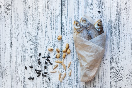 Three dried fish bream lie on a light wooden table. Fish wrapped in a paper bag. Near to lie pistachios and sunflower seeds.の写真素材