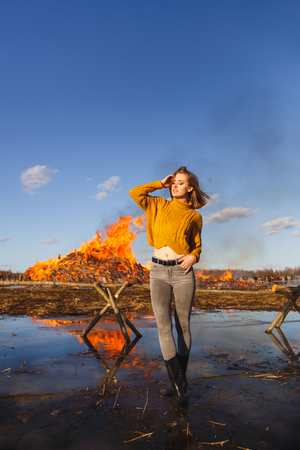 A girl in a yellow sweater with a short haircut stands on the background of a huge bonfire.の写真素材
