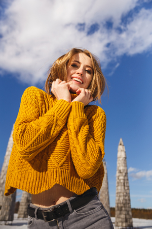 Russia, Kaluga region, Nikola-Lenivets - March 9, 2019: Maslenitsa week. Universal intelligence. A girl in a yellow sweater with a short haircut stands on the background of unusual wooden buildings.のeditorial素材