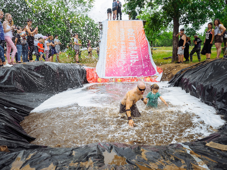 RUSSIA, Bryansk - June 30, 2018: Obstacle Race. Athletes in suits jump into a pit of water. Judge pours water running from a fire hose. Riddick and his sonのeditorial素材