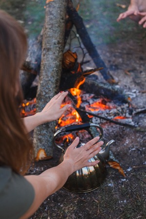 Girl warms her hands over the kettle by the fire.の写真素材