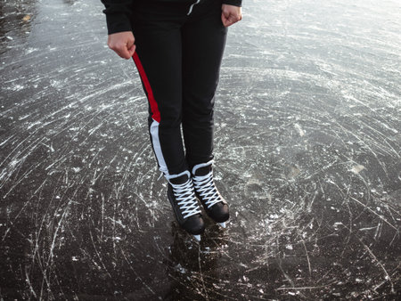 Legs of a girl in black hockey skates on the ice of a lake close-up. In the background a forest.