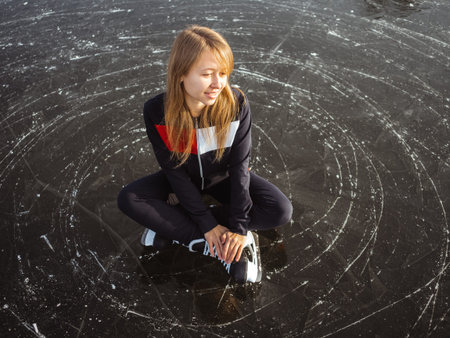 Young girl ice skating sits on the ice of a lake.