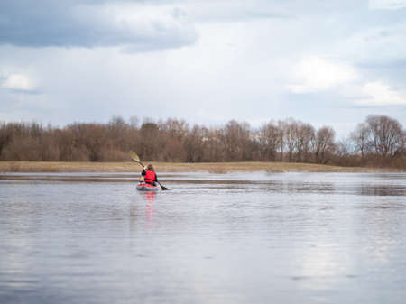 A girl with a dog on a red kayak swims in the distance on the horizon.の写真素材