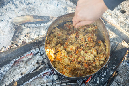 Camping black kettle with pilaf on the coals of a fire. Smoke from burning coalsの写真素材