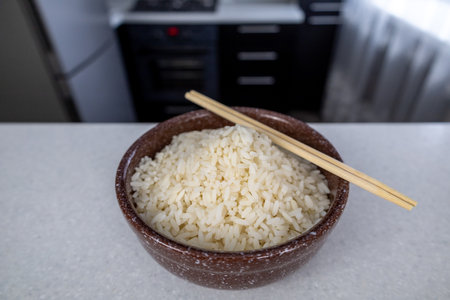 A plate of brown color with golden rice and chopsticks on the table against the backdrop of a dark kitchen. Asian food concept.の写真素材