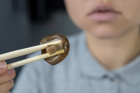 A girl in a gray shirt in the kitchen holds a shiitake mushroom with chopsticks. Asian food concept.