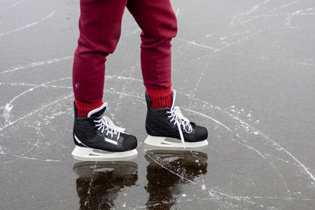 Black skates on ice. Women's legs in burgundy pants stand on the surface of a frozen forest lake.の写真素材