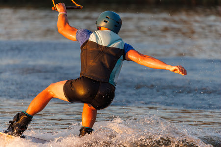 An athlete performs a trick on the water. Park at sunset. Wakeboard rider.の写真素材