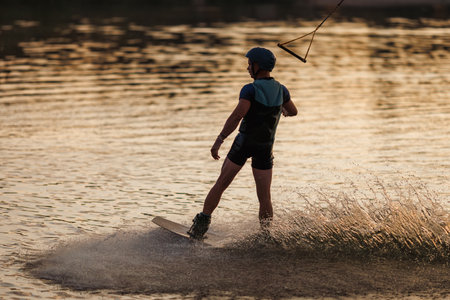 An athlete performs a trick on the water. Park at sunset. Wakeboard rider.の写真素材