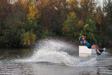 An athlete jumps from a springboard. Wakeboard park at sunset. A man performs a trick on a board.の写真素材