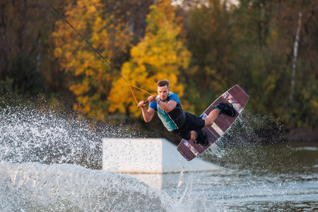 An athlete does a trick from a springboard. A rider jumps on a wakeboard against a background of a green forest. Sunset on the lake.の写真素材