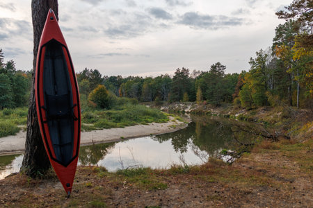 Camping on the bank of a forest river. Red Kayak against a background of water and trees. Tourist parking in the evening.の写真素材