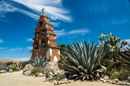 The historic belltower of Mission San Miguel Arcangel stands proudly amid cactus plants beneath a beautiful summer sky in California の写真素材