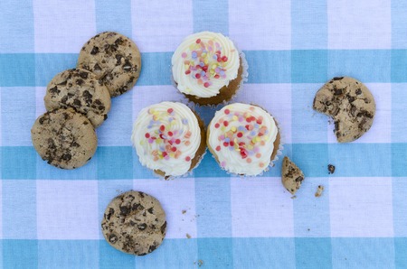 Tasty cookies and muffins with vanilla cream decorated with sugar candies in a wooden background. Sweet pastries cakes, biscuites, chocolate chipsの写真素材