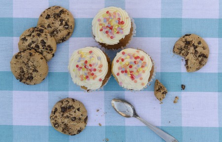 Tasty cookies and muffins with vanilla cream decorated with sugar candies in a wooden background. Sweet pastries cakes, biscuites, chocolate chipsの写真素材