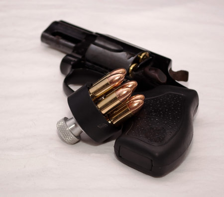 A black revolver with a loaded speed loader leaning against it on a white backgroundの写真素材