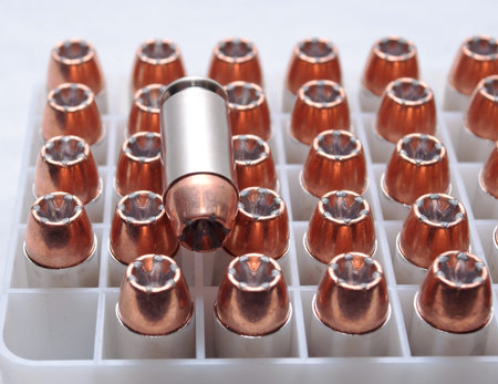 .40 caliber hollow point bullets in a plastic shell container with on bullet laying on top of them