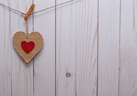 A single brown heart with a smaller red heart in it;s center hanging on a line in front of a white wooden fenceの写真素材