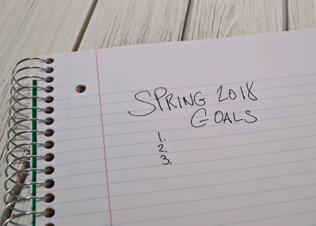 Spring 2018 to do list written on a white notebook in black ink with the notebook laying on a white wooden tableの写真素材
