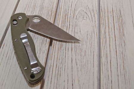 An opened folding pocket knife with a green handle laying on a white wooden tableの写真素材