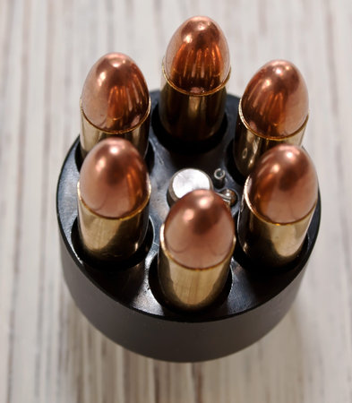 A close up top view of a revolver's speed loader, loaded with six bullets sitting on a white wooden...
