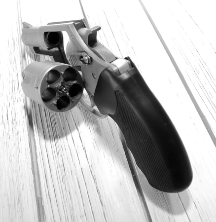 A stainless steel unloaded revolver on a wooden table with it's cylinder opened showing it's opened.の写真素材